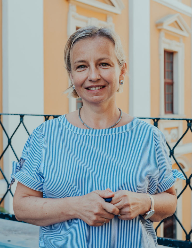 dr hab. Anna Majewska-Tworek, prof. UWr - uśmiechnięta kobieta w jasnych długich spiętych włosach na tle budynku Wydziału Filologicznego